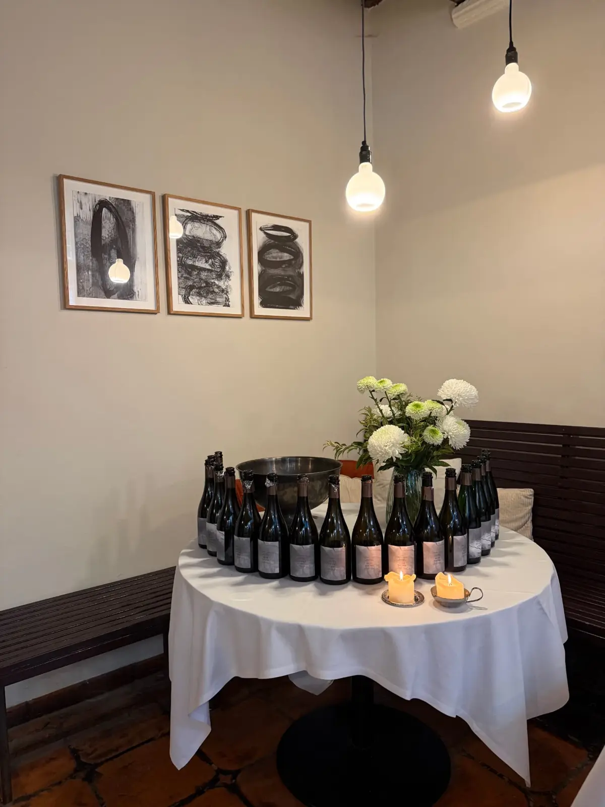 Ronde tafel vol wijnflessen onder hangende lampjes
